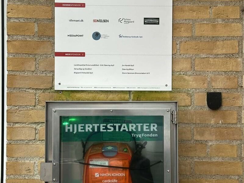 Hjertestarter på muren med sponsortavlen, hvor MEDIAPOINT står som hovedsponsor